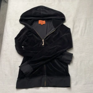 Svart velour hoodie Juicy Couture S - Svart hoodie från Juicy Couture i mjuk velour med glittrande J-dragkedja. Klassisk huva, ribbade muddar och hel dragkedja framtill. Perfekt för dig som gillar ikonisk Y2K-stil och vill ha något riktigt comfy och snyggt. 💕