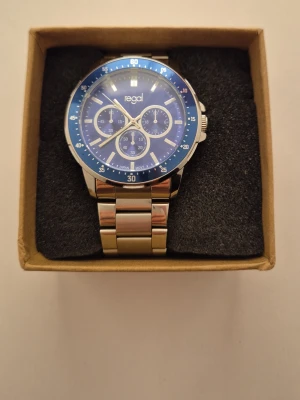 Regal blå och silverfärgad klocka - Stilren klocka med blå urtavla, silverfärgade detaljer och länkarmband i metall. Klockan har flera små urtavlor och markerad blå ram runt glaset. Perfekt accessoar för dig som gillar en sportig men klassisk look.