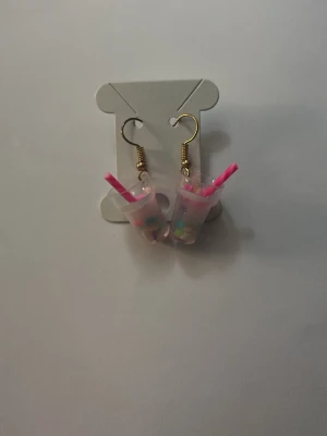 Örhängen med bubbelte-motiv - Roliga örhängen formade som små bubbelte-muggar med rosa sugrör och färgglada pärlor inuti. Krokarna är i guldfärgad metall och muggarna är gjorda av plast. Perfekt accessoar för dig som älskar unika och lekfulla smycken.