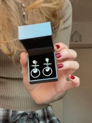 Silvriga örhängen med cirklar och kristaller - Snygga silvriga örhängen med glittrande stenar och hängande cirklar. Örhängena har en modern design med en liten pärlliknande detalj i mitten av cirkeln. Perfekta för att lyfta din stil med en trendig touch. Tror ej de är äkta silver men de har aldrig irriterat mina öron eller gett utslag.