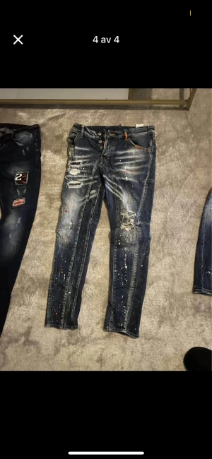 Mörkblå distressed skinny jeans - Säljer ett par mörkblå skinny jeans med slitningar, färgstänk och tvättade detaljer. Jeansen har knappgylf och klassisk femficksmodell. Perfekt för dig som gillar en edgy och trendig stil.
