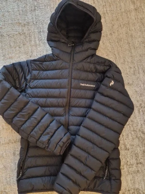 Peak Performance jacka - Säljer en svart Peak Performance dunjacka med huva (herrmodell) i storlek S. Jackan är använd endast ett fåtal gånger och är i ett väldigt bra skick. Inga hål, fläckar eller slitningar. Säljs pga att den snabbt blev för liten. Nypris 2 399 kr