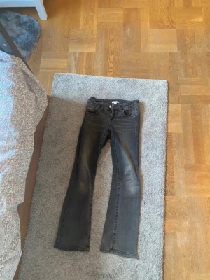 Gråsvart bootcut jeans med slitningar - Säljer ett par grå bootcut jeans med lätt slitna detaljer och klassisk femficksmodell. Jeansen har en något utsvängd passform nedtill och är perfekta för en avslappnad men ändå trendig look. Materialet är denim i bomull.storlek 158