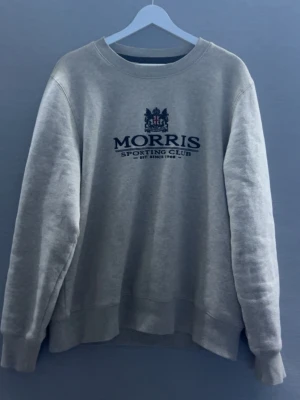 Beige tröja (Morris) - Snygg grå sweatshirt från Morris med tryck 'Morris Sporting Club' och emblem på bröstet. Tröjan har rund halsringning, ribbade muddar och är tillverkad i mjukt material som känns skönt mot huden. Perfekt för en avslappnad och stilren look.