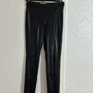 Svarta leggings i skinnimitation från MNG - svarta leggings i skinnimitation från MNG. De har en tight passform och hög midja, perfekt för en trendig look. Materialet är glansigt och ger en cool känsla. Passar dig som gillar stilrena och moderna plagg.