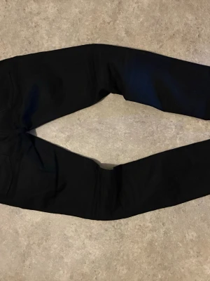 Svarta jeans från Nudie Jeans - Säljer ett par svarta skinny jeans från Nudie Jeans med klassisk femficksmodell och silverfärgade nitar. Jeansen har smal passform och är tillverkade i stretchigt denimtyg för extra komfort. Perfekta för en clean och stilren look.