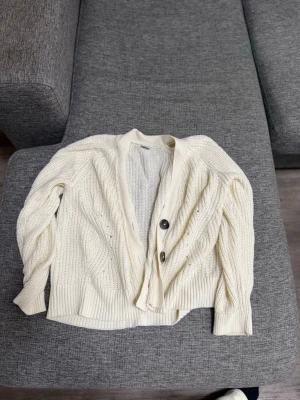 Krämvit stickad kofta med knappar - Säljer en krämvit stickad kofta med tre stora svarta knappar framtill. Koftan är från Lindex i storlek 146/152 men passar mig som bär Xs-S. 