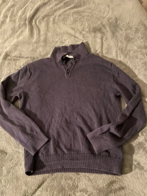 Mörkblå tröja med krage från Zara - Mörkblå långärmad tröja från Zara med hög krage och två knappar vid halsen. Tröjan har ribbade muddar vid ärmslut och nederkant, vilket ger en snygg och avslappnad look. Perfekt för dig som gillar stilrena och enkla plagg. Liten i storlek, skriv för fler frågor