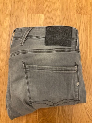 Grå jeans från Replay - Snygga grå jeans från Replay med klassisk femficksmodell och raka ben. Jeansen har en diskret tvättad look och svart patch med Replay-logga bak i midjan. Tillverkade i mjukt denimtyg som ger en skön känsla och stilren vibe. Slim fit. 