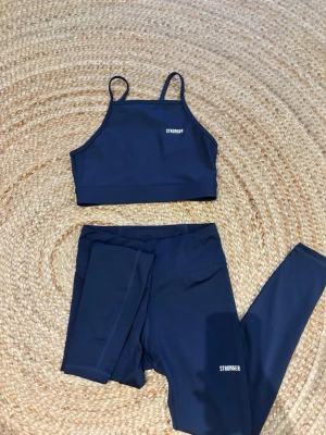 Mörkblått träningsset från Stronger - Snyggt mörkblått träningsset från Stronger med sport-bh med smala axelband och matchande tights i stretchigt funktionsmaterial. Perfekt för gymmet eller löprundan. Diskret logga på både bh och byxa. Ficka bak i ryggen på byxorna, se bild 3. Aldrig använda. 