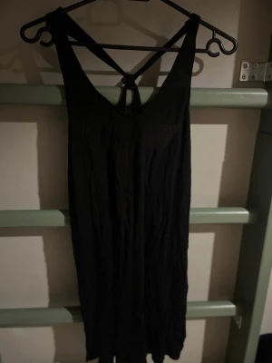 Svart ärmlös linnetopp med knyt - Säljer en svart ärmlös linnetopp med snygg knytning i ryggen och djup urringning. Toppen har en lös passform och tunna axelband som korsas i ryggen. Perfekt för en avslappnad och trendig stil.