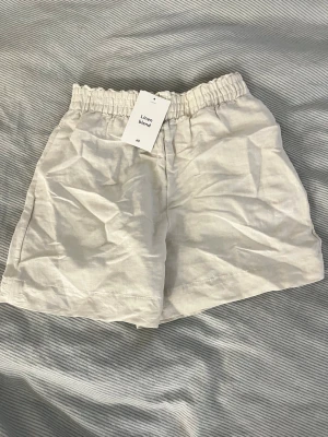 Beiga linneshorts från H&M - Snygga och luftiga beiga shorts från H&M i linnemix. De har elastisk midja för extra komfort och en avslappnad passform. Perfekta för varma dagar när du vill ha något stilrent och bekvämt.