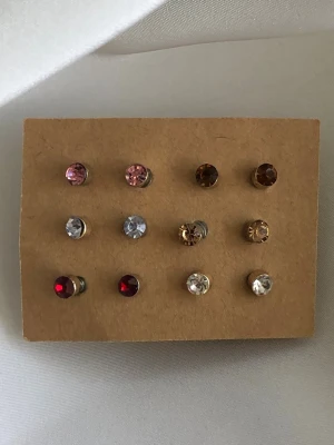 Små örhängen olika färger - Små örhängen i guldfärg med små syntetiska stenar i olika förger för att matcha olika outfits. 