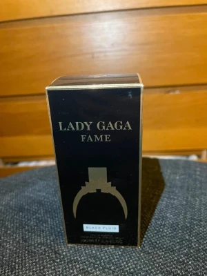 Lady Gaga Fame parfym 100ml - Discontinued Lady Gaga Fame parfym med svart och guldig design. Flaskan har en unik oval form med guldfärgat lock och detaljer, och innehåller den ikoniska Black Fluid-doften. Förpackningen är svart med guldfärgade inslag och text. OBS! Öppnat förpackning men ej använt flaska.