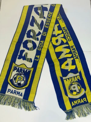 Blågul halsduk Parma Calcio - Snygg blå och gul halsduk med Parma Calcio-logga och texten 'Forza Parma' samt 'La gioia di essere gialloblu'. Halsduken har fransar i ändarna och är perfekt för att visa ditt stöd för laget. 