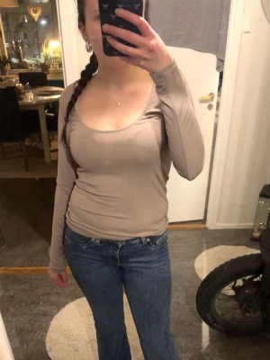Beige långärmad topp med rund hals - Snygg beige långärmad topp med rundad halsringning. Toppens passform är tight och den är enkel att matcha till olika outfits. Perfekt basplagg för garderoben.