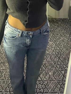 Ljusblå raka jeans med hög midja - Säljer ett par ljusblå jeans med rak passform och klassisk femficksdesign. Jeansen har hög midja och stängs med dragkedja och knapp. Perfekta för en avslappnad och trendig look. Materialet är denim i bomull.