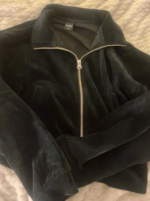 Svart ziptröja från Topten - Mörk, sammetslen ziptröja från Topten med hög krage och silverfärgad dragkedja. Tröjan har en avslappnad passform och är perfekt för en chill och stilren look. Materialet är mjukt och ger en lyxig känsla. Från Sydkorea.  Använt en gång tror jag eftersom prislappen är bort tagen. Passar mig som har xxs-xs 