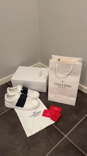 Valentino - Säljer ett par snygga Valentino Garavani Open sneakers i vitt med bred marinblå rem över snörningen. Riktigt feta och mycket bra skick. Tillverkade i skinn och kommer med originalkartong, dustbag och äkthetskort. Bara att höra av sig vid funderingar 🙌