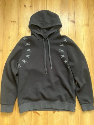 Neil Barrett hoodie, strl L - Svart hoodie från Neil Barrett med ikoniska blixtar i grått/svart över axlarna. Banden är lite noppriga, i övrigt fint skick. 
