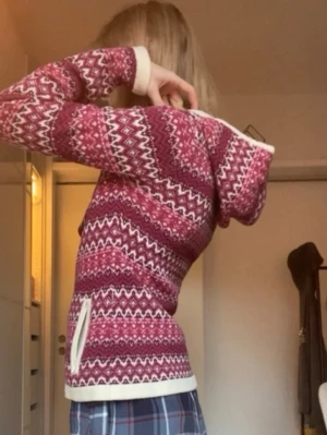 Tight mönstrad zip-kofta, jumperfabriken - Stickad hoodie från jumperfabriken i olika nyanser av rosa och vitt med klassiskt nordiskt mönster. Tröjan har huva, långa ärmar och vita ribbade muddar vid ärmslut och nederkant. Perfekt för kalla dagar och riktigt mysig stil. Den är ull och såå varm. Köpt här på vinted för ca 600kr och endast använd en gång av mig.