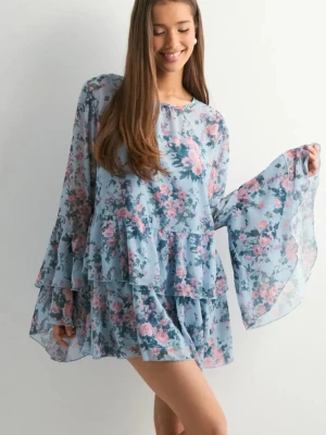 Blommig volangklänning i blått - Söt kort blommig klänning i ljusblått med rosa och gröna blommor. Klänningen har långa vida ärmar och flera volanglager som ger en romantisk känsla. Perfekt för sommarens varma dagar.