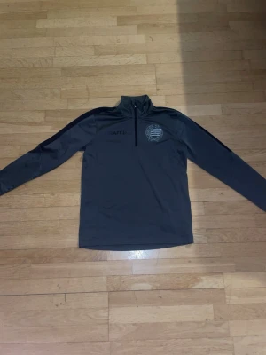 Grå träningströja Hammarby  - Schysst långärmad träningsjacka från Craft med halv dragkedja och Bajen-loggan på bröstet. Storlek XS men sitter bra på S