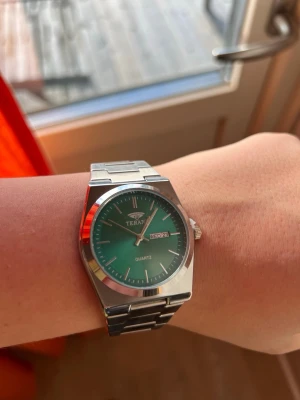 Grön TERAN Quartz klocka i stål - Stilren klocka från TERAN med grön urtavla och dag/datumvisning. Boett och länk i silverfärgat rostfritt stål. Klassisk design med kvartsverk och tydliga indexmarkeringar. Perfekt accessoar för dig som gillar en modern look.