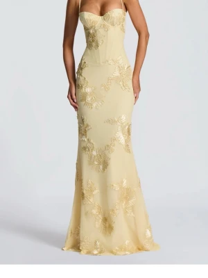 Gul maxiklänning med spetsdetaljer - Elegant gul maxiklänning med tunna axelband, figurnära passform och blommiga spetsapplikationer. Klänningen har en korsettinspirerad överdel och öppen rygg med snörning. Perfekt för dig som vill sticka ut på bal eller fest. HELT NY endast testad. Från babyboo