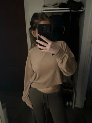 Beige croppad sweatshirt - Trendig beige croppad sweatshirt med rund hals och långa ärmar. Perfekt för en avslappnad och stilren look. Mjuk och skön, passar till både jeans och mjukisbyxor.