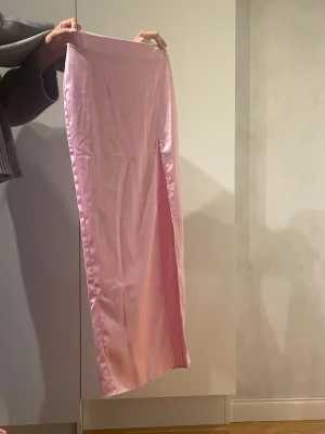 Rosa lång satinkjol med slits - Snygg rosa långkjol i satin med hög slits framtill. Kjolen har en rak passform och en glansig finish som ger en trendig look. Helt oanvänd 
