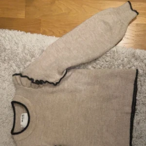 Beige stickad tröja med volang från Selected Femme - Säljer en beige stickad tröja från Selected Femme i storlek S. Tröjan har svarta detaljer vid halsringning, ärmslut och nederkant samt en snygg volang längs axeln. Perfekt för dig som gillar stilrena plagg med en twist. Endast använd ett fåtal gånger så den är som ny! Skicka dm ifall ni har fler frågor eller vill ha fler bilder!💓köparen står för frakten! 💓