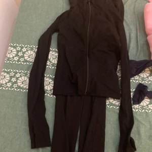 Svart sportig hoodie med dragkedja - Svart, figurnära hoodie med dragkedja framtill och långa ärmar. Jackan har en enkel och stilren design, perfekt för en sportig look. Mjuk och stretchig känsla, passar bra till träning eller chill. Ett set från gin med yoga pants och jacket
