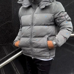 Grå pufferjacka från WUS - Säljer en grå pufferjacka från WUS med coola färgstänk i vitt, blått och rött. Jackan har hög krage, huva och dragkedja framtill. Perfekt för dig som vill sticka ut med en unik vinterjacka. Fickor med dragkedja och en schysst oversized vibe.