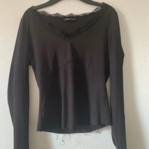 Svart långärmad topp med spets - Svart långärmad topp från SHEIN med v-ringning och spetsdetaljer längs halsringningen. Toppen är ribbad och har en lätt croppad passform, perfekt för att lyfta en enkel outfit.
