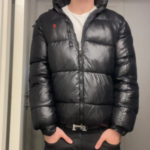 Svart pufferjacka från Polo Ralph Lauren - Säljer nu min Polo Ralph Lauren puffer jacka (glansig)  Jackan är endast använd en vinter och är i topp skick, jag är 183 cm och väger 80 kg. Storlekek på jackan är Large. Tveka inte på att höra av dig ifall du har några frågor!