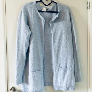 Ljusblå kofta från ICHI med fickor - Blå, lång kofta från ICHI i mjuk polyesterblandning. Koftan har två stora fickor framtill, ribbade muddar och är öppen framtill utan knäppning. Perfekt för lager-på-lager och chill dagar.