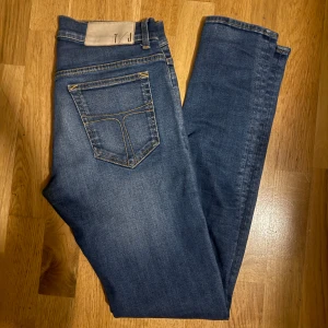 Tiger of Sweden slim jeans 29/32 - Säljer ett par blå skinny jeans från Tiger of Sweden med klassisk femficksdesign, gul kontrastsöm och läderpatch med logga bak. Jeansen har smal passform och är tillverkade i stretchigt denim för en bekväm känsla.
