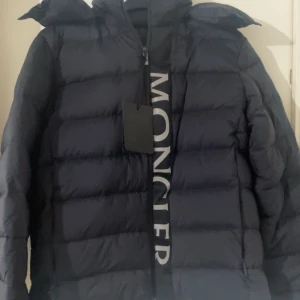 Mörkblå dunjacka från Moncler - Snygg och varm mörkblå dunjacka från Moncler med dragkedja och huva. Perfekt för kyliga dagar med sin quiltade design och långa ärmar. Moncler-logga synlig på framsidan. Storlek M passar L pris kan diskuteras 