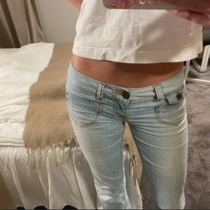 Ljusblå bootcut jeans från Only - Säljer ett par ljusblå jeans från Only med låg midja och bootcut-ben. Jeansen har klassiska fem fickor, snygga detaljer med dubbla knappar framtill och ljusa slitningar. Perfekta för dig som gillar en avslappnad och trendig look.
