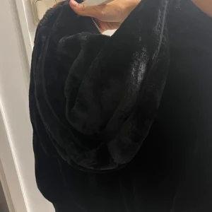 Svart pälsjacka från Bershka - Mysig svart pälsjacka från Bershka med dragkedja framtill. Jackan har lång ärm, mjuk fuskpäls och en lite croppad passform. Perfekt för dig som vill ha en stilren och trendig look med extra fluff.