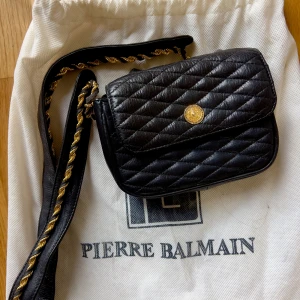 Vintage Pierre Balmain flap bag 1980s-1990s - Elegant and timeless vintage Pierre Balmain quilted leather shoulder bag, dating from the late 1980s to early 1990s. Black leather with the house’s signature diamond quilting, it features a gold-tone chain and removable leather shoulder strap, and a Pierre Balmain gold medallion clasp on the front flap.  Inside, the bag is lined in black satin repeatedly printed with Pierre Balmain, and includes the original black-and-gold Balmain fabric label. Comes with the original dust bag. 