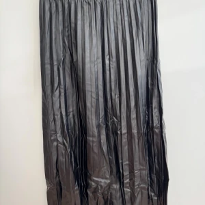 Svart plisserad midikjol från ASOS - Svart plisserad midikjol från ASOS DESIGN i storlek 34/XS. Kjolen har en elastisk midja och är tillverkad av 93% polyester och 7% elastan. Har aldrig använts, men har ett märke på högra sidan som fanns redan vid leverans. 