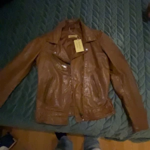 Brun skinnjacka från Divided - Snygg brun skinnjacka från Divided med klassisk bikerkrage och dragkedjor framtill. Jackan har långa ärmar och två fickor med dragkedja. Perfekt för dig som vill ha en cool och tidlös look.