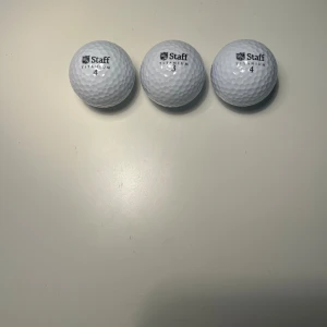 Staff Titanium Golfbollar - Tre Staff Titanium golfbollar i mycket gott skick. Bollarna är rena, vita och utan synligt slitage eller skador. Perfekta för både träning och tävling. Nummer 3 och 4. Säljes som set.Nytt skick på bollarna men paketet kan vara lite slitage vid öppningen.