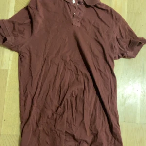 Vinröd pikétröja från Pier One - Säljer en vinröd pikétröja från Pier One med klassisk krage och knappar framtill. Tröjan är i mjuk bomull och har korta ärmar, perfekt för en avslappnad och stilren look. Passar dig som gillar enkel och tidlös stil.