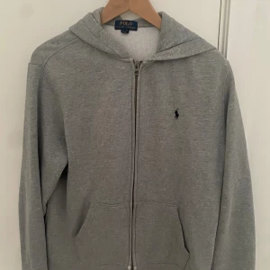 Grå zip-hoodie från Polo Ralph Lauren XS - Klassisk grå zip-hoodie från Polo Ralph Lauren i storlek XS. Använt den sparsamt vilket har resulterat i att den fortfarande är i väldigt fint skick. Säljer den på grund av att den blivit lite för liten. Nypris: 1 195kr