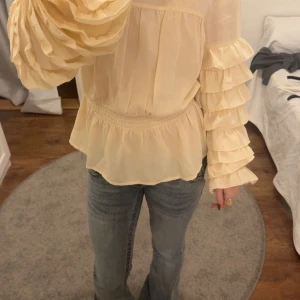 Beige volangblus med puffärmar - Supersöt beige blus med volangdetaljer på ärmarna och puffiga långärmar. Ser gul ut men är inte det. Perfekt till fest, säljs pga används inte.