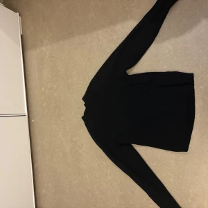 Svart ribbad stickad tröja - En svart, ribbad stickad tröja med lång ärm och hög hals. Perfekt för lager-på-lager och passar till allt. Enkel och stilren design som funkar till jeans eller kjol.