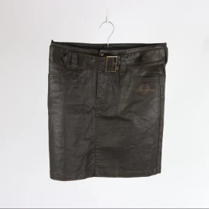 Brun kortkjol med bälte från Chevalier - Snygg brun kortkjol från Chevalier med ett brett bälte och metallspänne i midjan. Kjolen har raka linjer, fickor fram och en diskret slits bak.